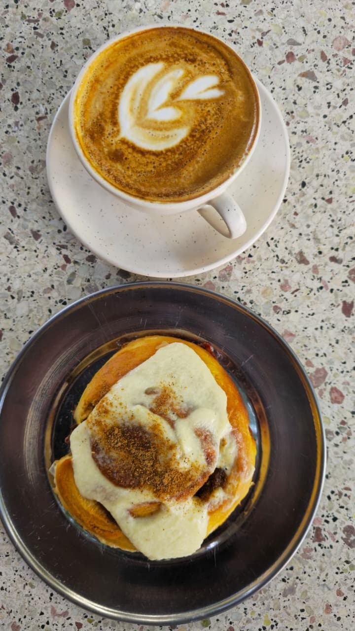 Latte y roll de canela vistos desde arriba en mesa de mármol