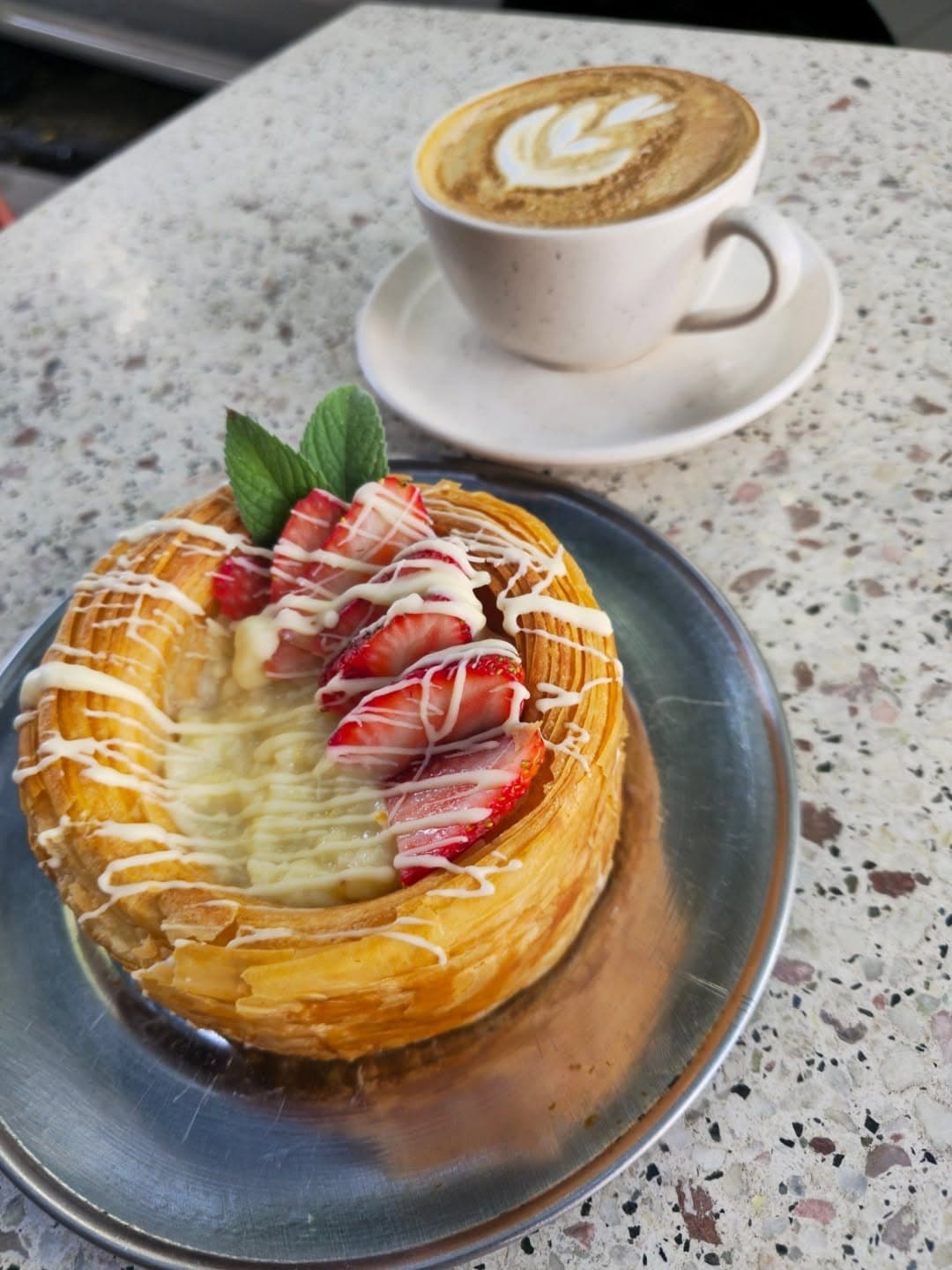 Pastelería con crema y frutilla junto a un latte